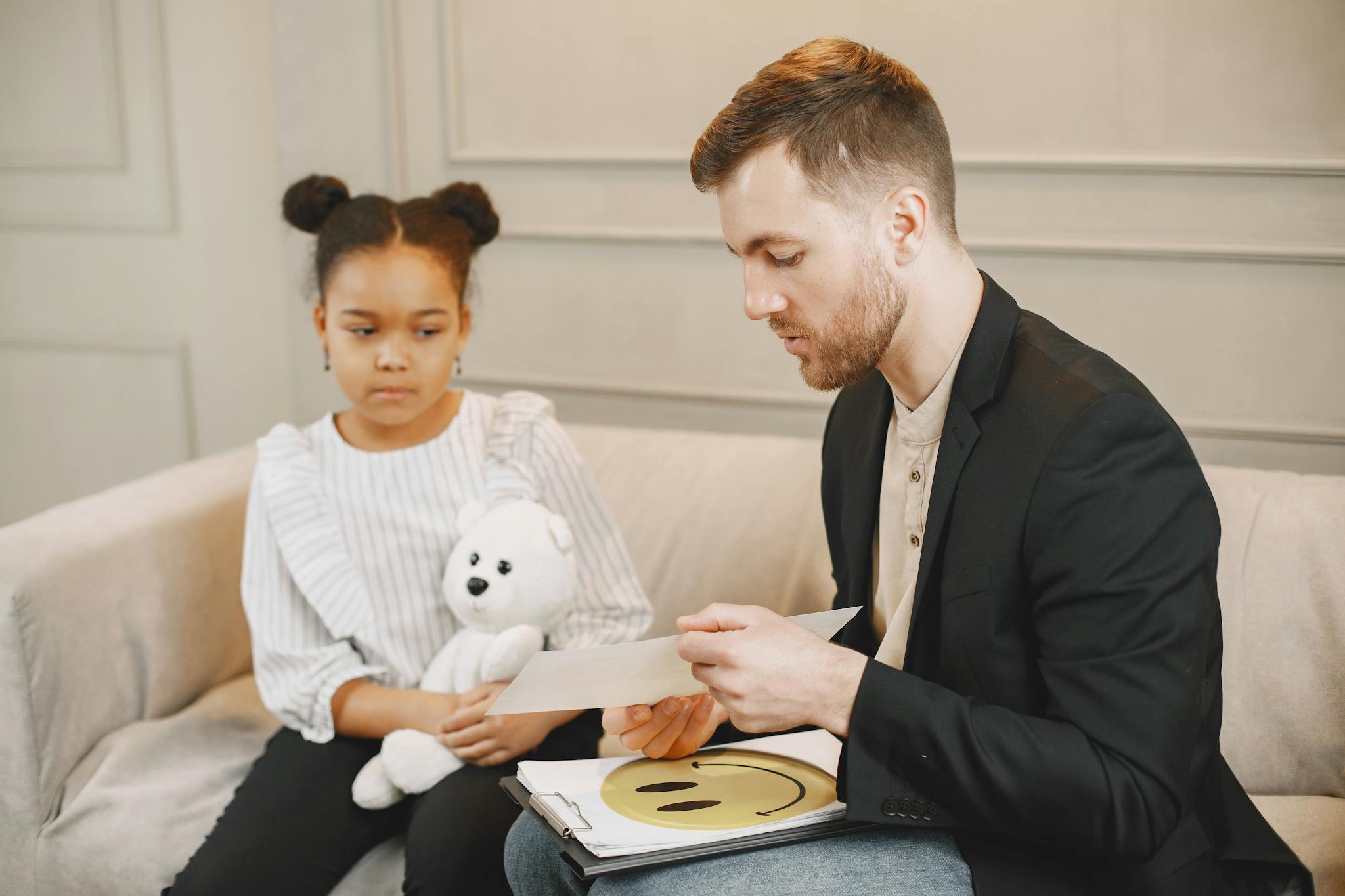 A child holding a plush toy listens to a man in a therapy session.